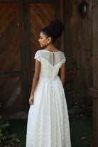 Woman in a white lace dress standing against a wooden wall.