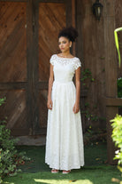 Woman in a white dress standing in front of a wooden door with greenery around.