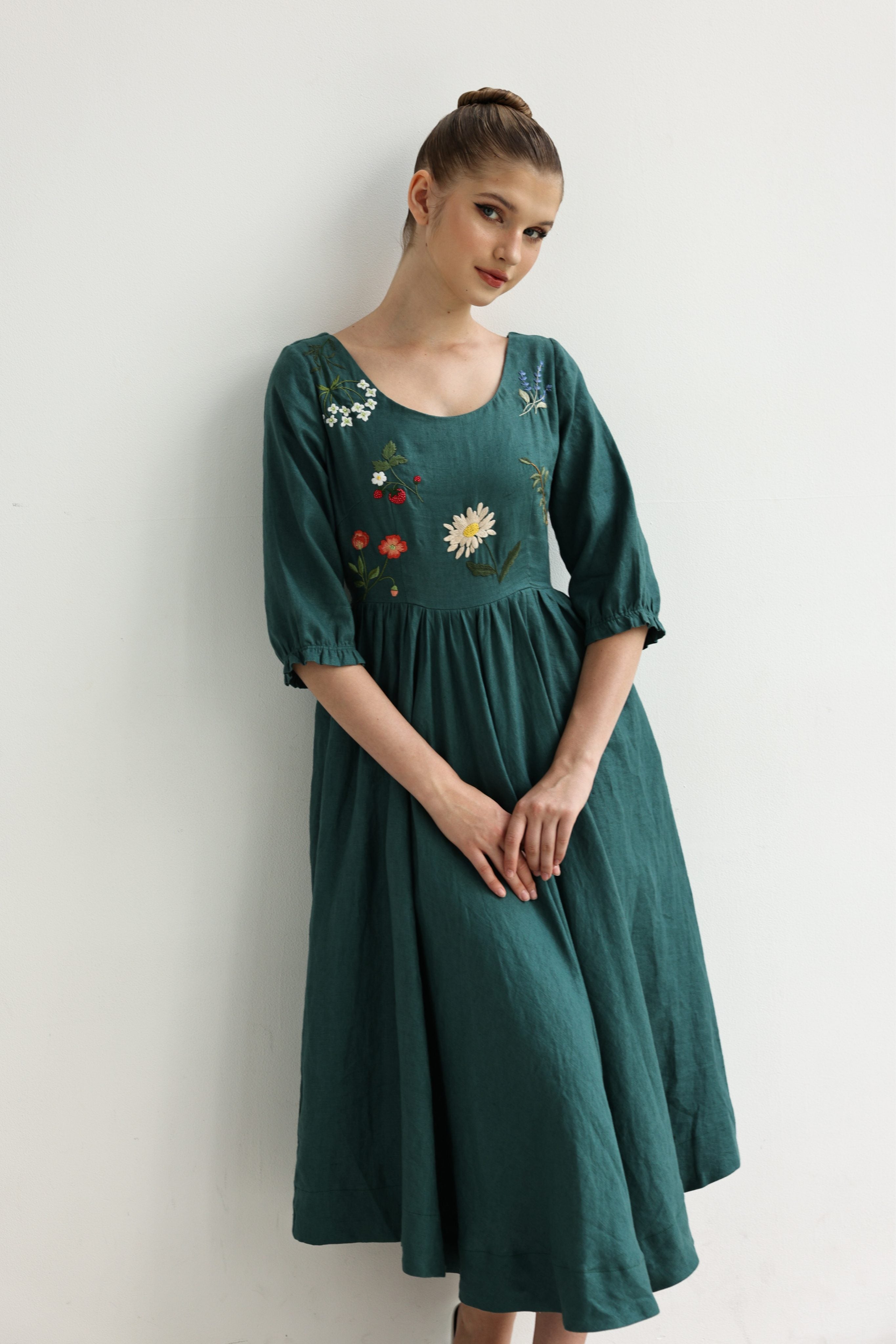 Woman wearing a green dress with floral embroidery against a white background