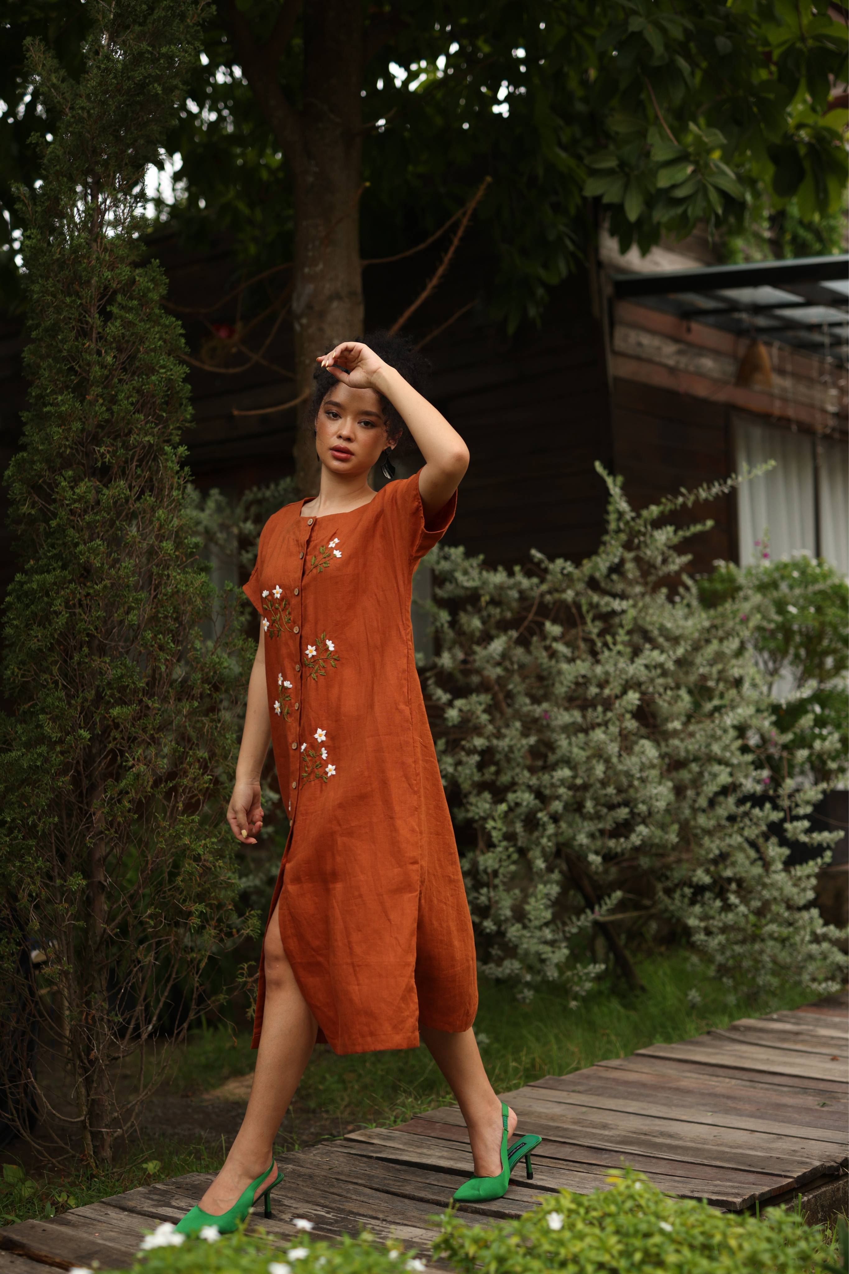 Woman in a dress standing on a wooden path with green shoes in a garden setting