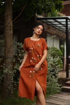 Woman wearing a rust-colored dress with floral embroidery in an outdoor setting