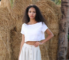 Woman in a white top and light-colored skirt standing in front of hay bales.