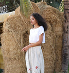 Woman in a white top and light pants standing next to hay bales.
