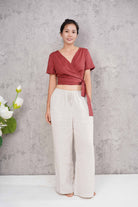 Woman wearing a red top and white pants against a gray concrete wall.