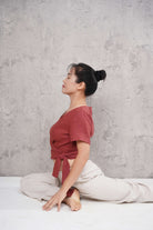 Woman in a red top and white pants sitting on a white floor against a gray wall.