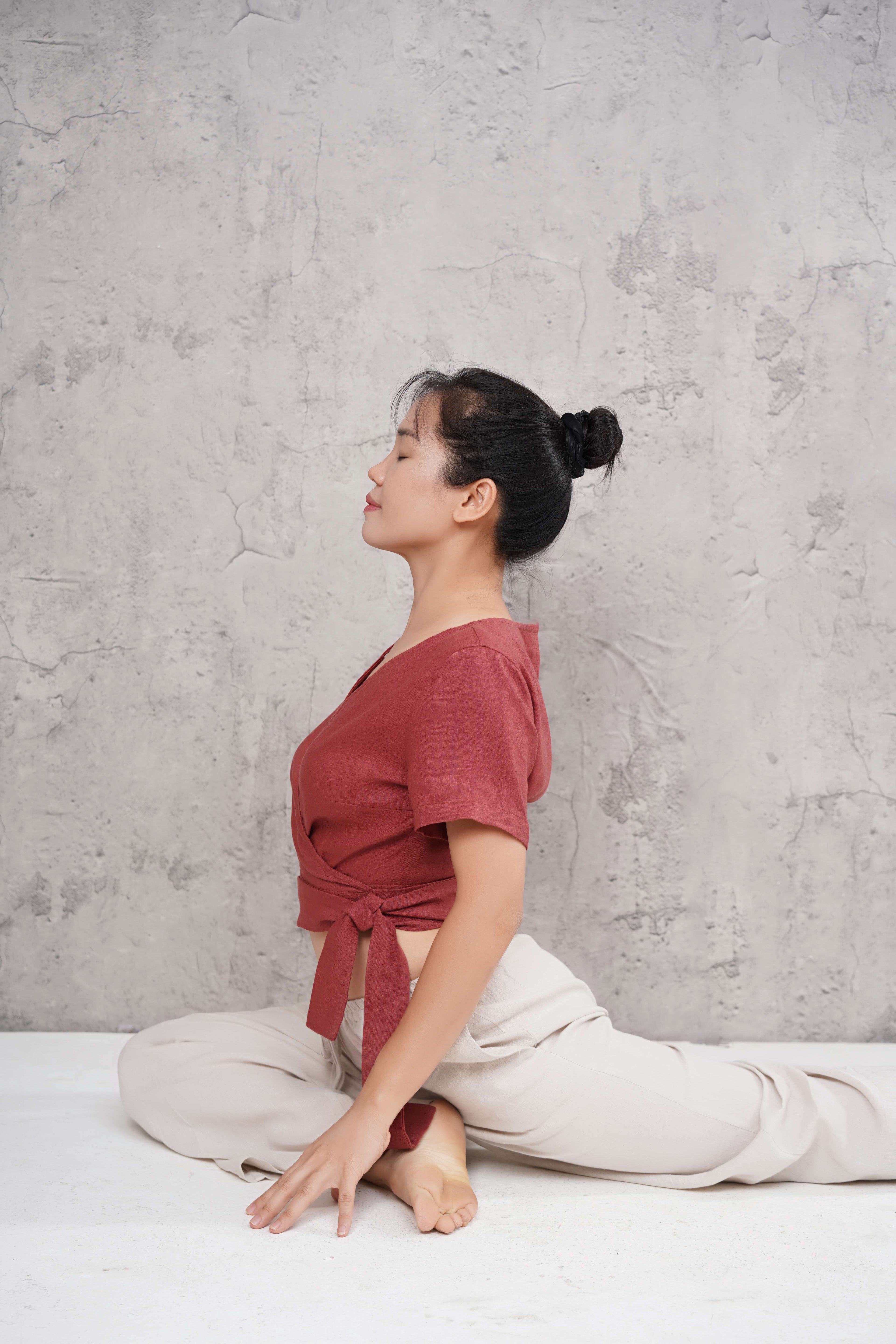 Woman in a red top and white pants sitting on a white floor against a gray wall.