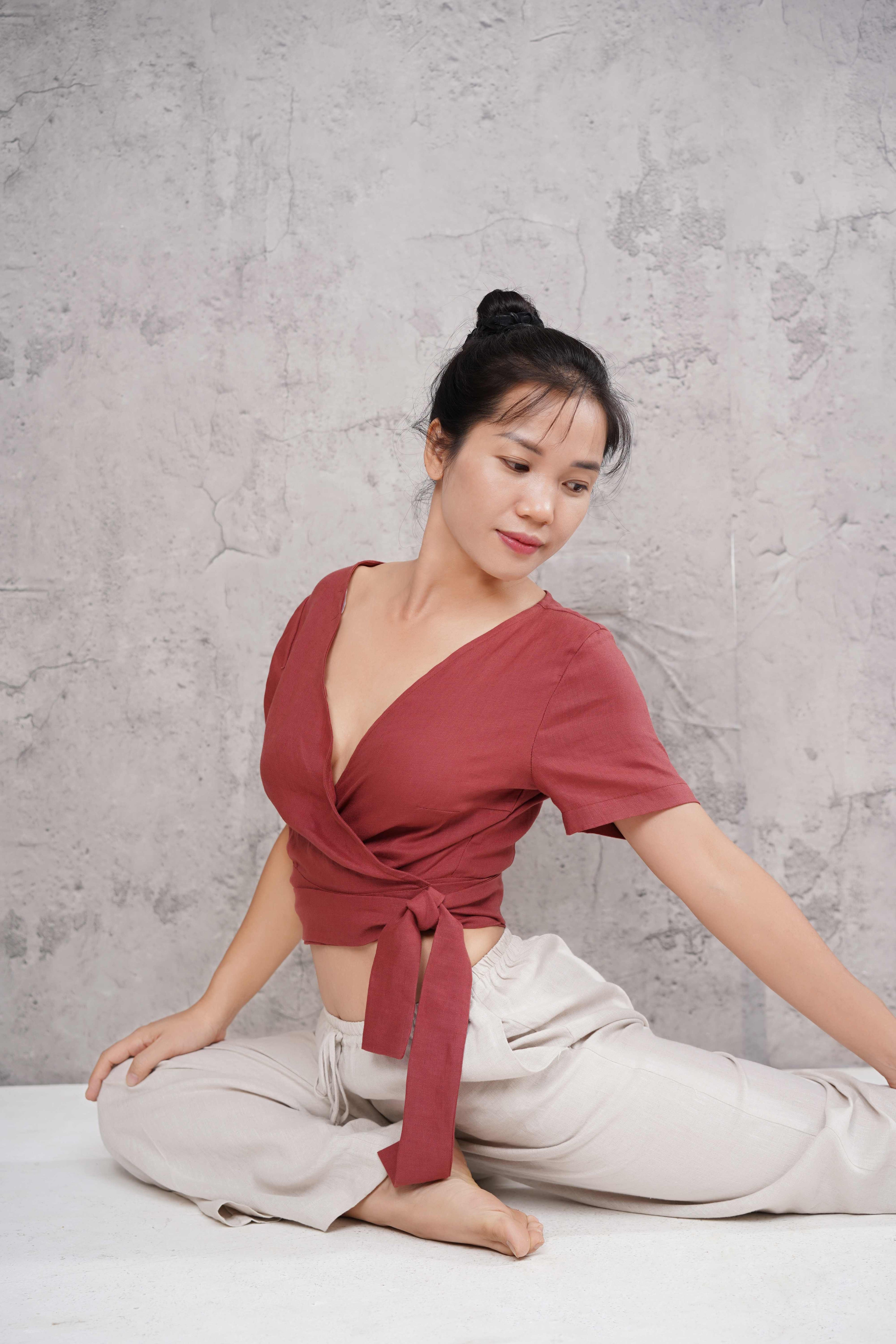 Woman in a red top and light pants sitting on a white surface with a gray textured wall background