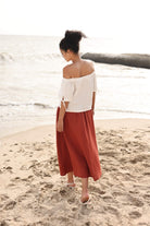 Woman in a white top and red skirt standing on a beach.