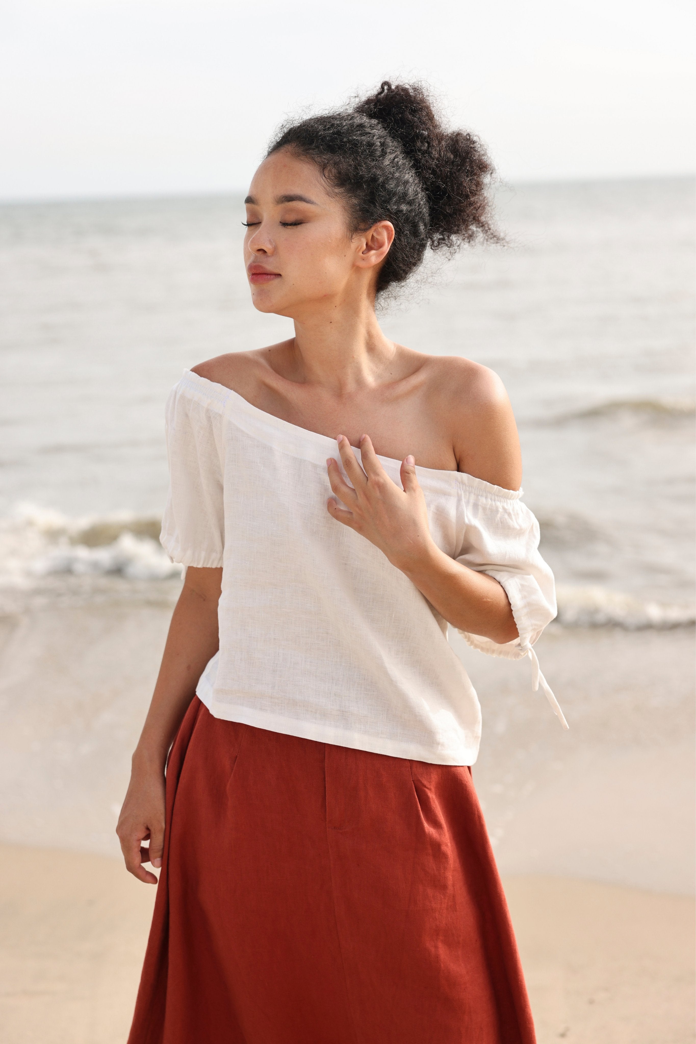 Woman in a white top and red skirt standing on a beach.