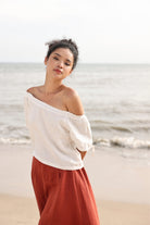 Woman wearing a white off-shoulder top and red skirt standing on a beach.