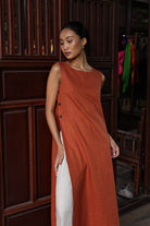 Woman wearing a long rust-colored dress with a wooden panel background