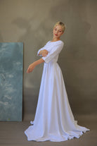 Woman in a white dress standing against a plain background