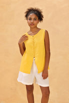 Woman wearing a yellow sleeveless top and white shorts against a beige background