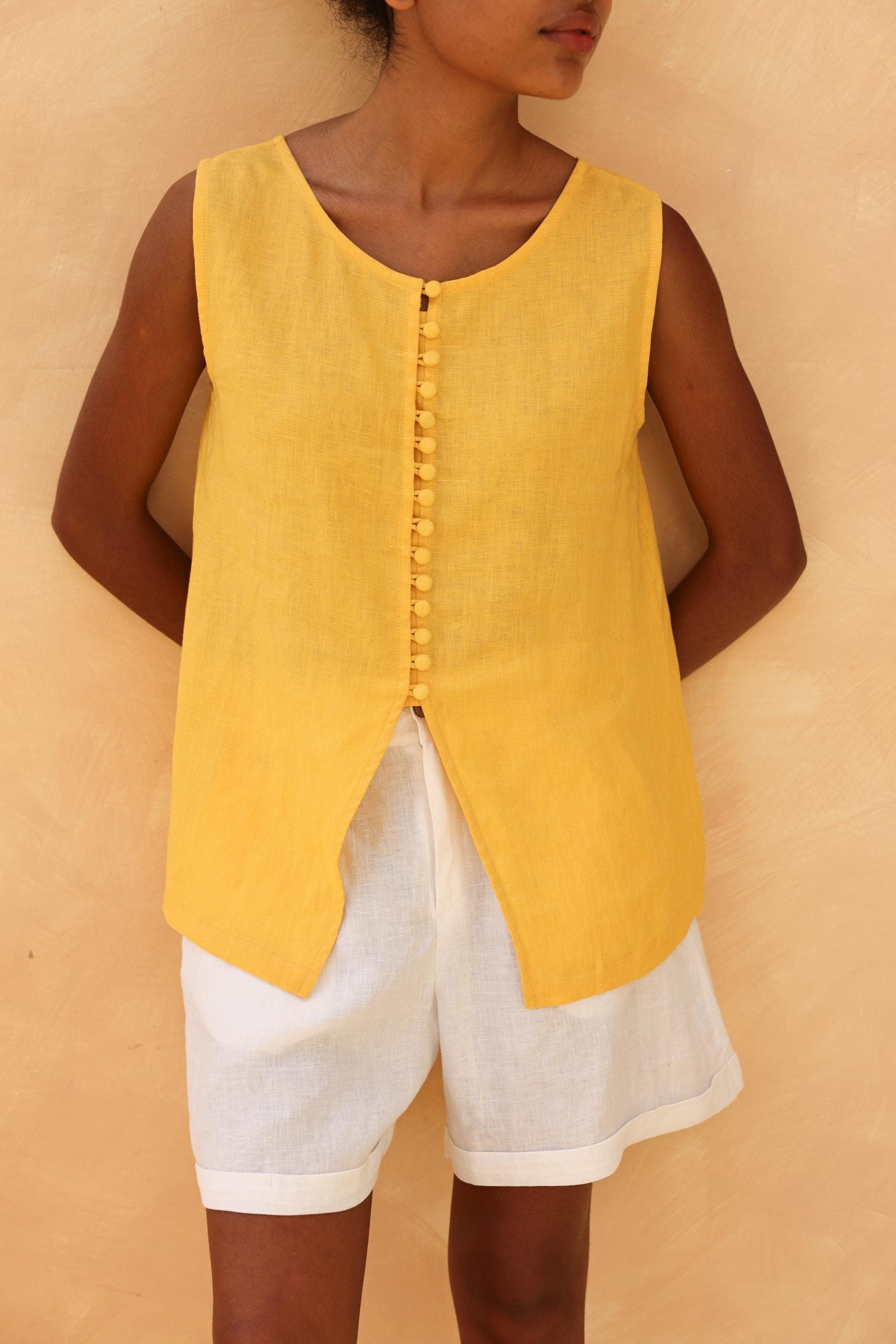 Person wearing a yellow sleeveless top and white shorts against a beige background