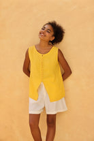 Woman wearing a yellow sleeveless top and white shorts against a beige wall
