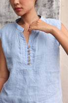 Light blue sleeveless top with button details worn by a person, against a neutral background.