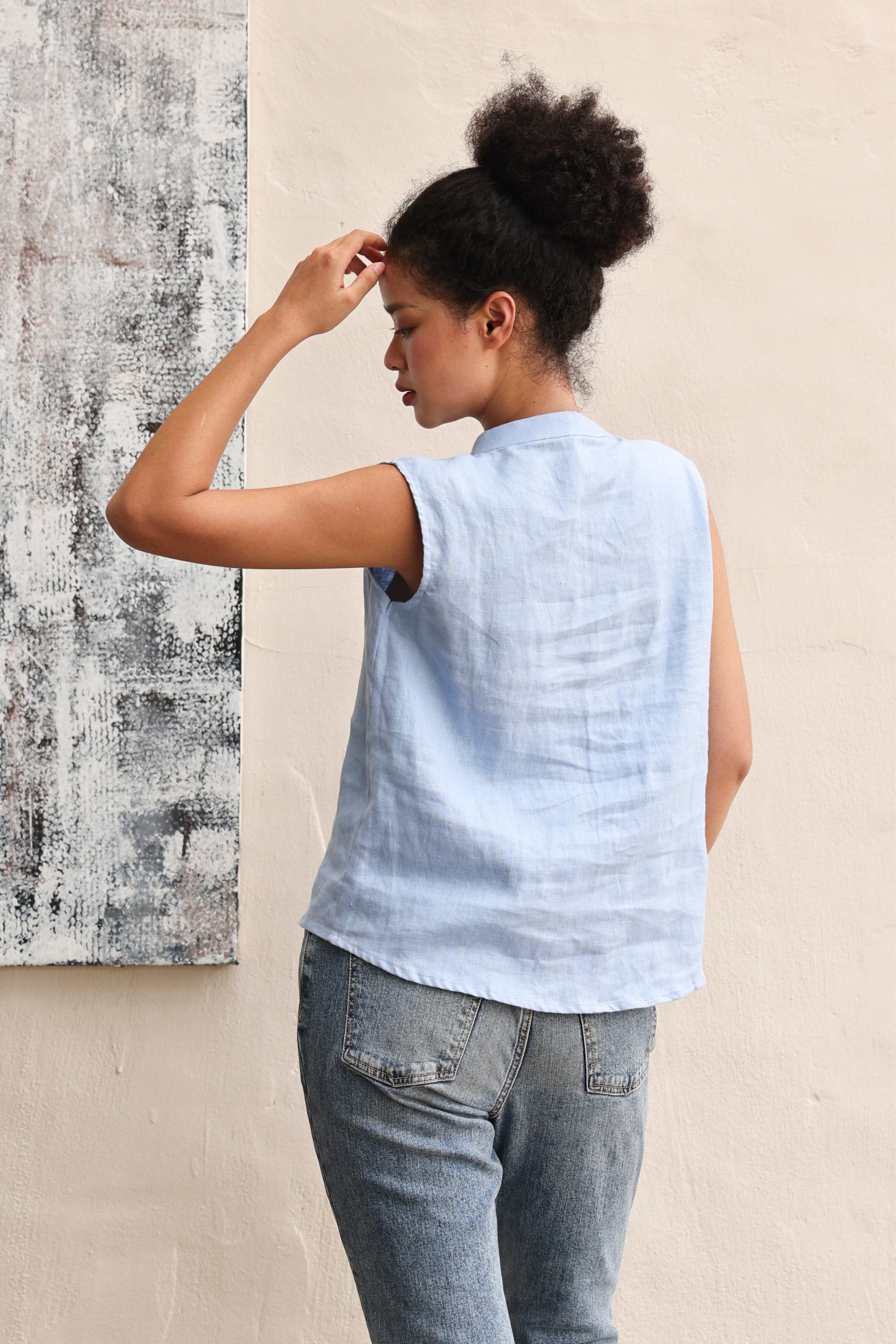 Woman wearing a light blue sleeveless top and pants against a beige wall.