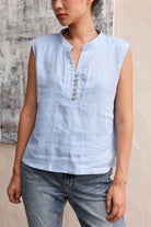 Woman wearing a light blue sleeveless top with buttons against a neutral background