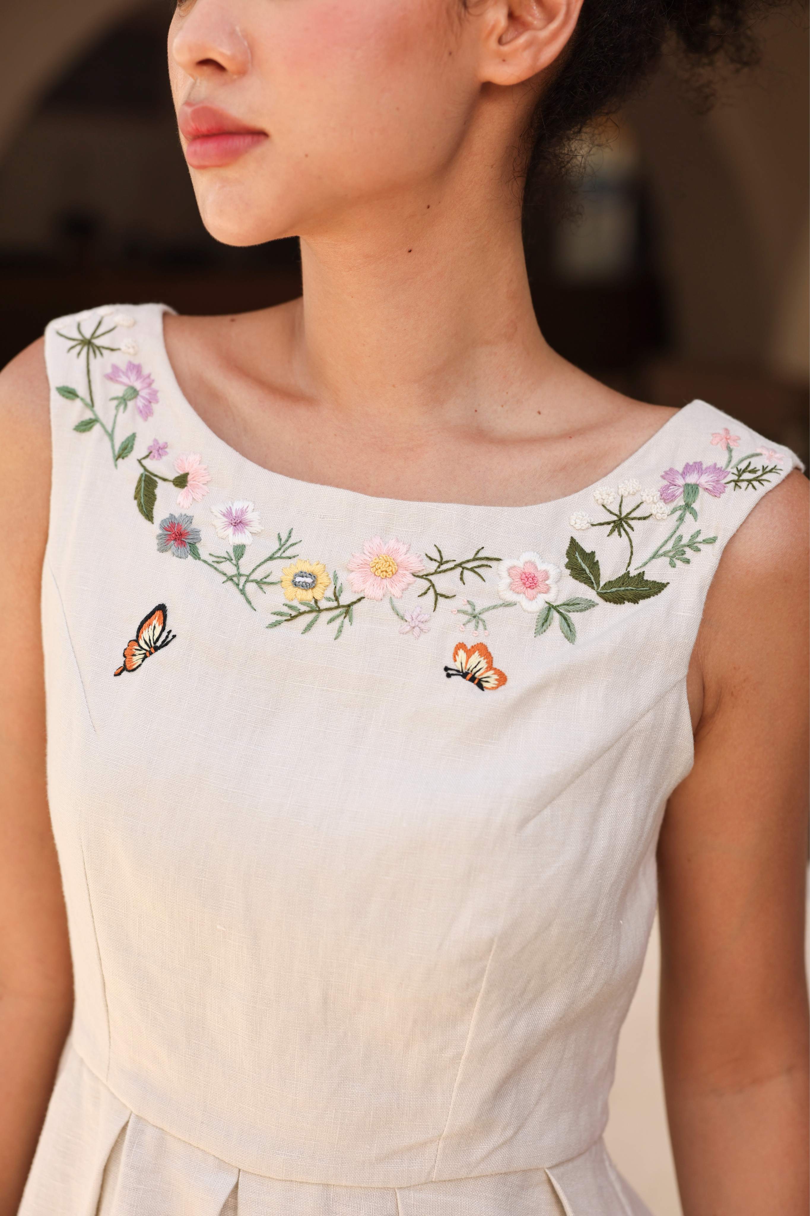 A sleeveless dress with floral embroidery and butterfly designs on a blurred background