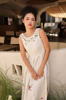 Woman in a dress with floral embroidery sitting on a bench outdoors.
