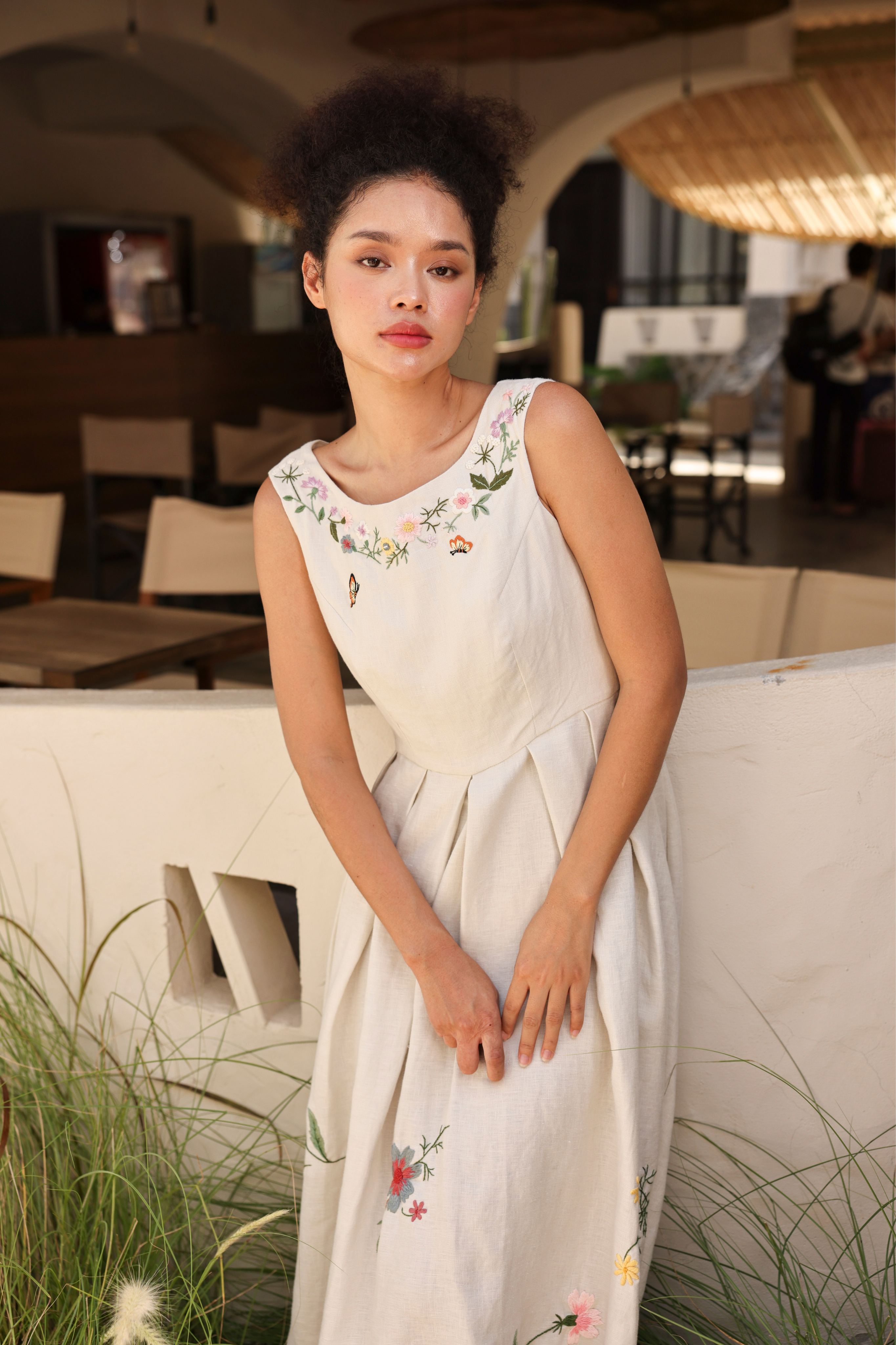 Woman in a dress with floral embroidery sitting on a bench outdoors.