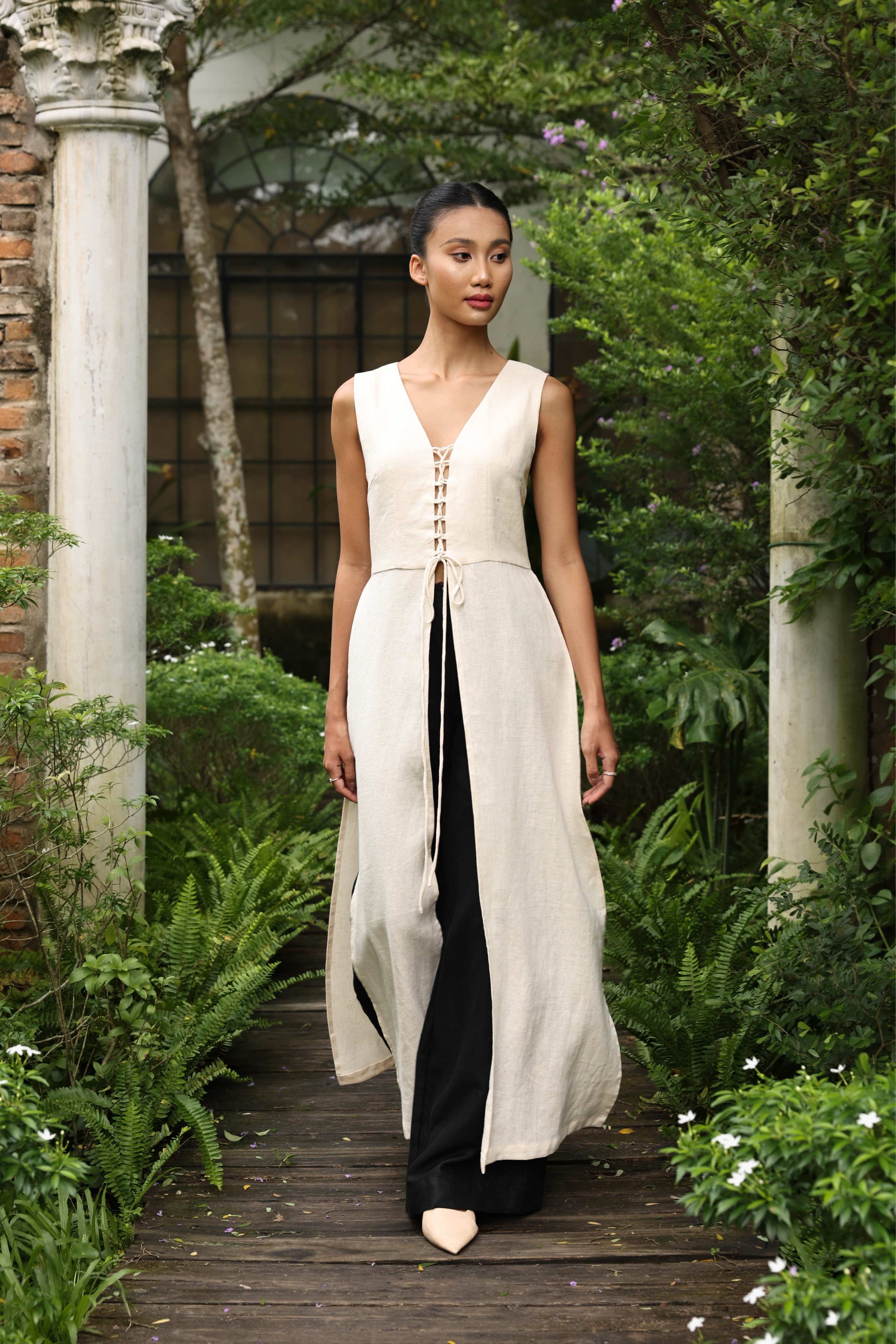 Woman in a white tunic and black pants standing in a garden setting