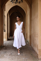 Woman in a white dress standing in an arched stone corridor.