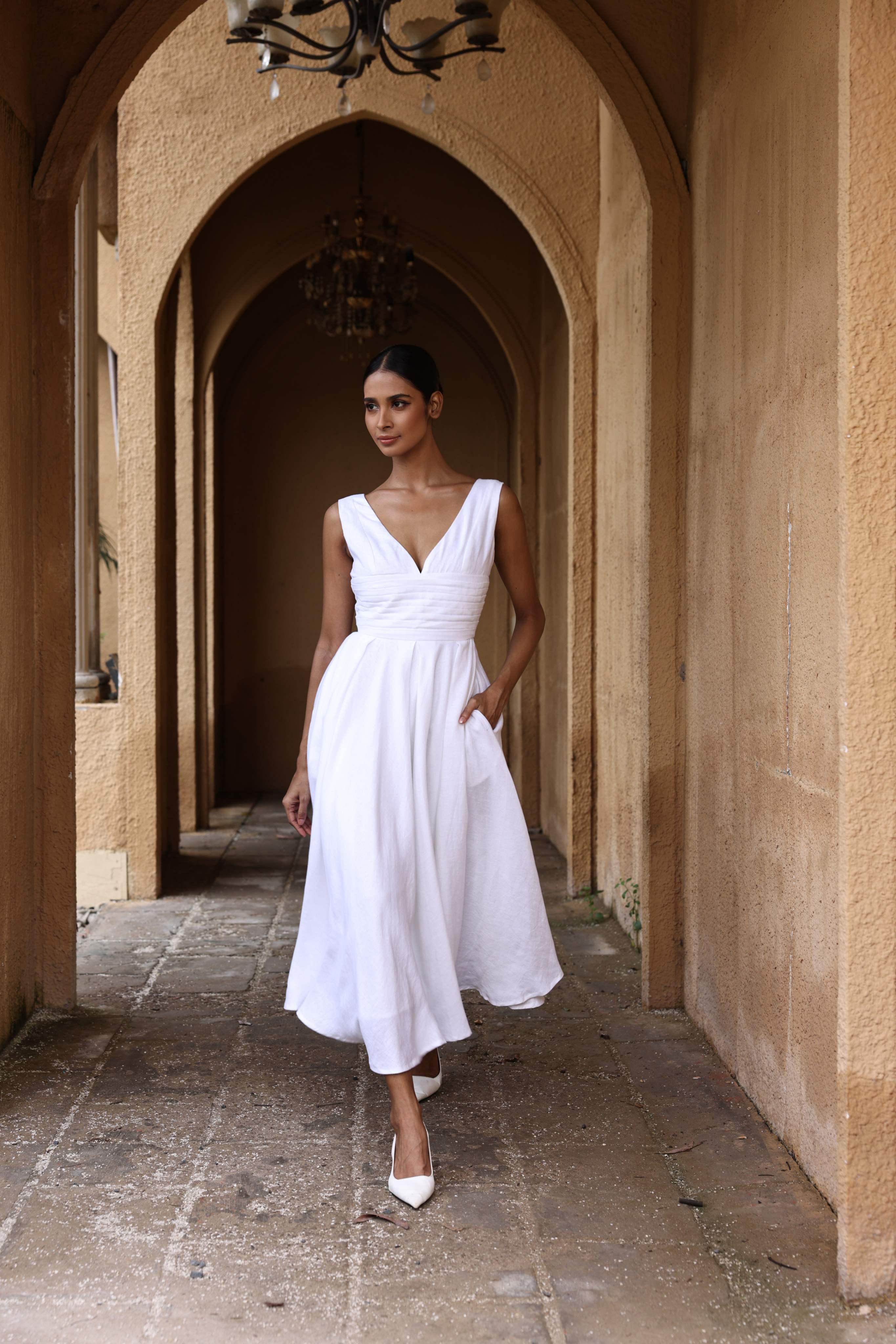 Woman in a white dress standing in an arched stone corridor.