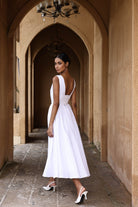 Woman in a white dress standing in an arched hallway with beige walls.