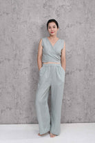 Woman wearing a sleeveless top and wide-leg pants against a concrete wall.