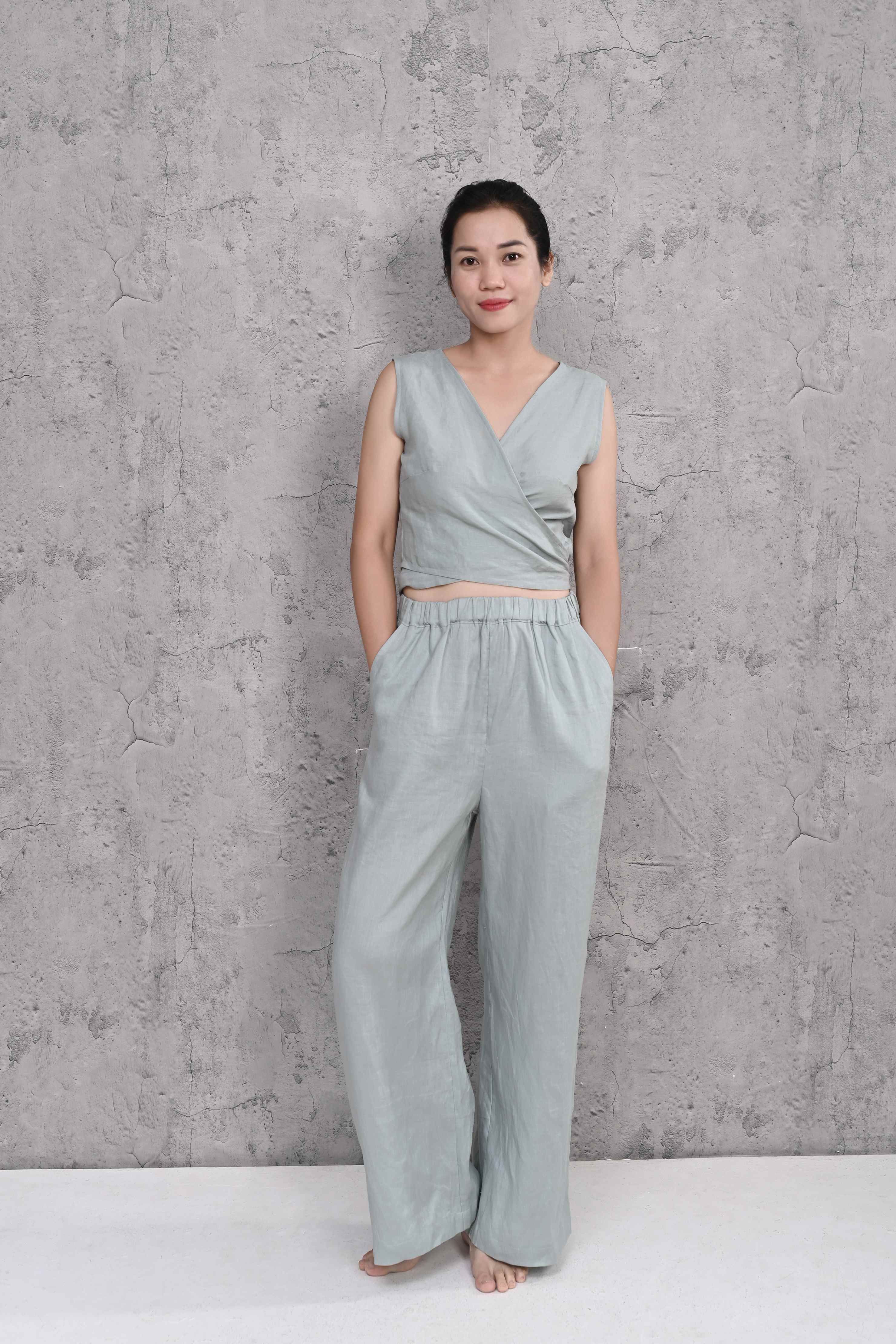 Woman wearing a sleeveless top and wide-leg pants against a concrete wall.