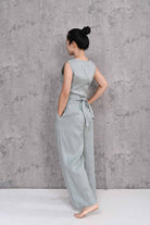 Woman wearing a sleeveless top and pants against a gray concrete wall.