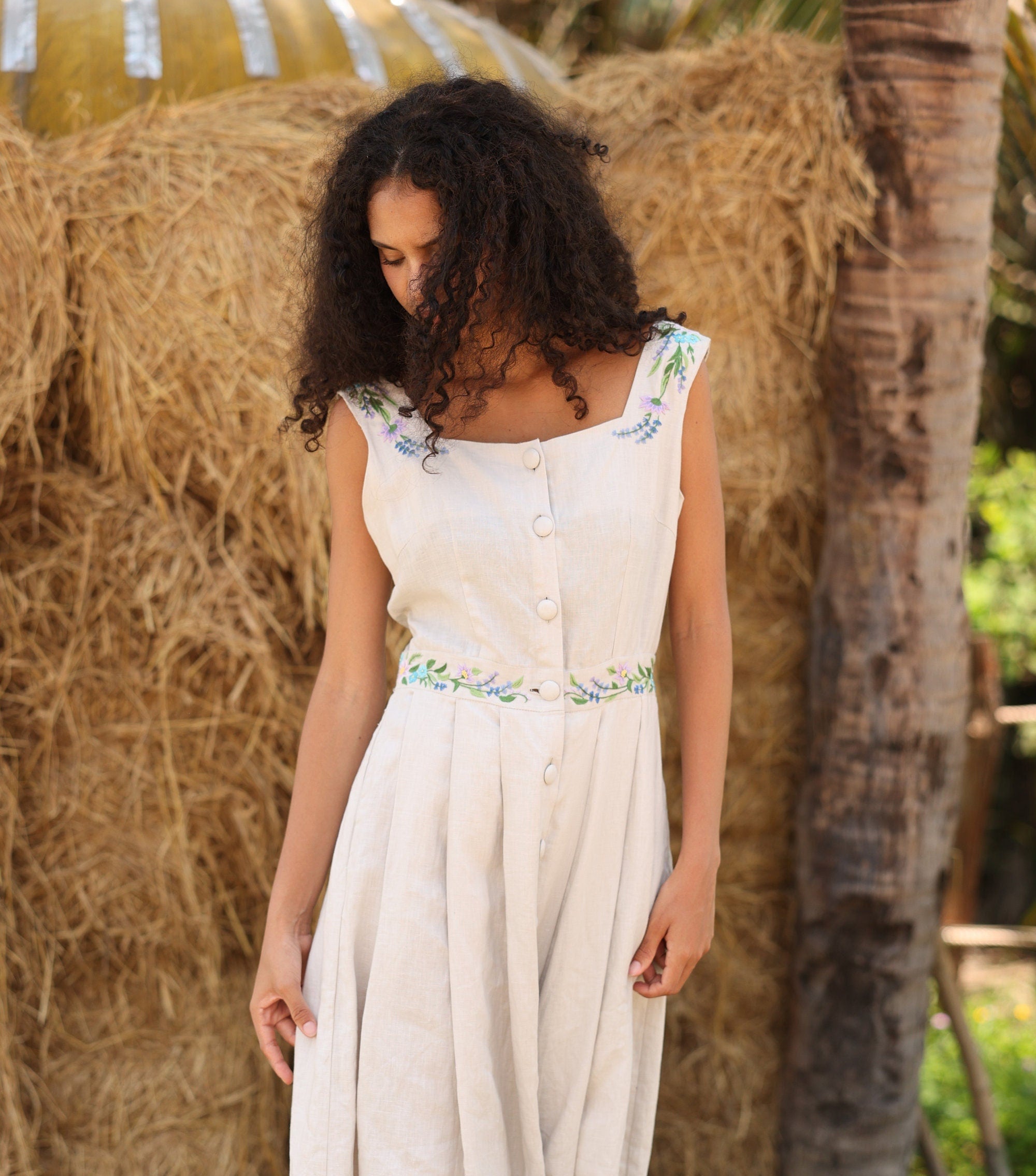 Woman in a dress with floral details standing in front of hay bales.