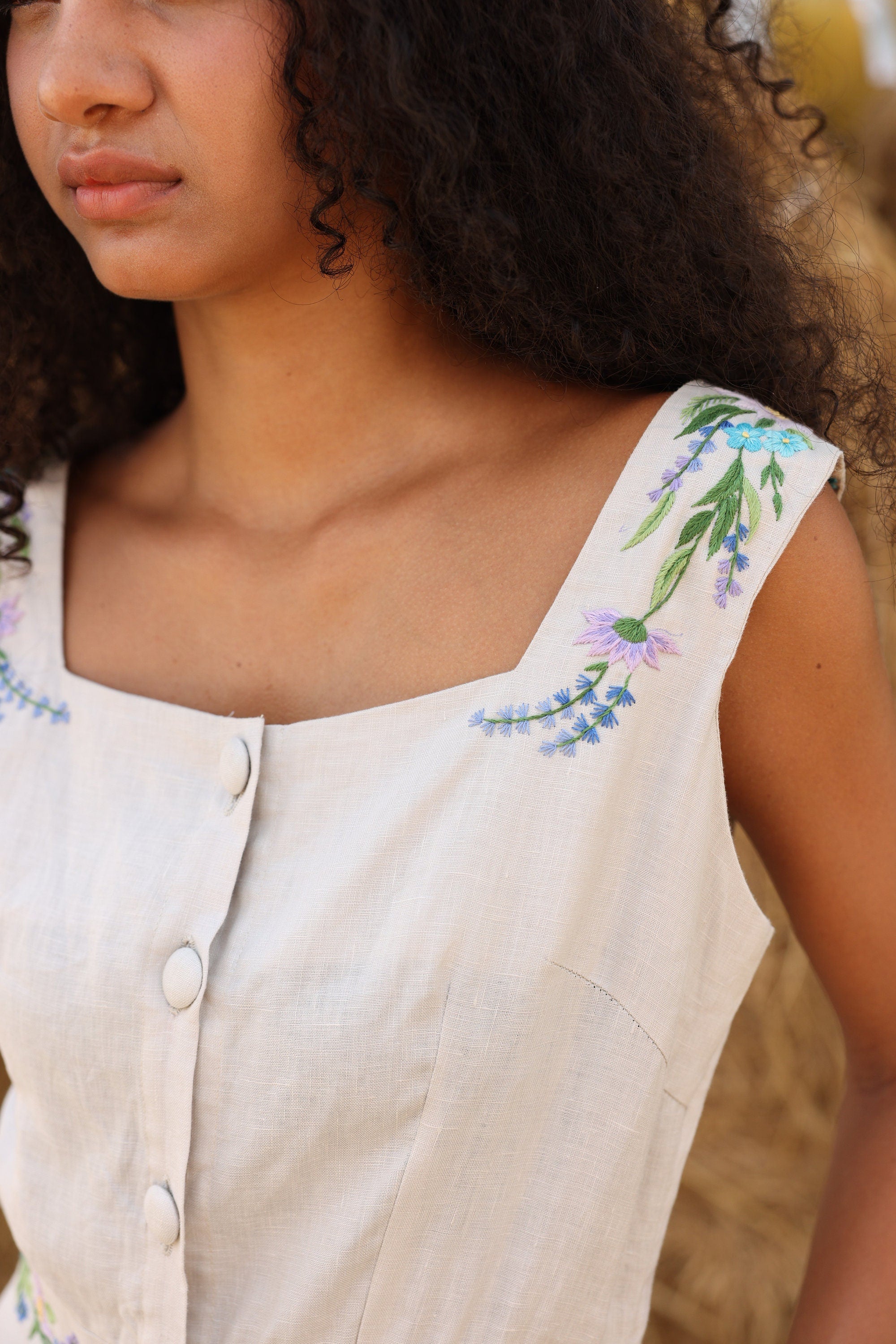 Woman wearing a beige sleeveless top with floral embroidery