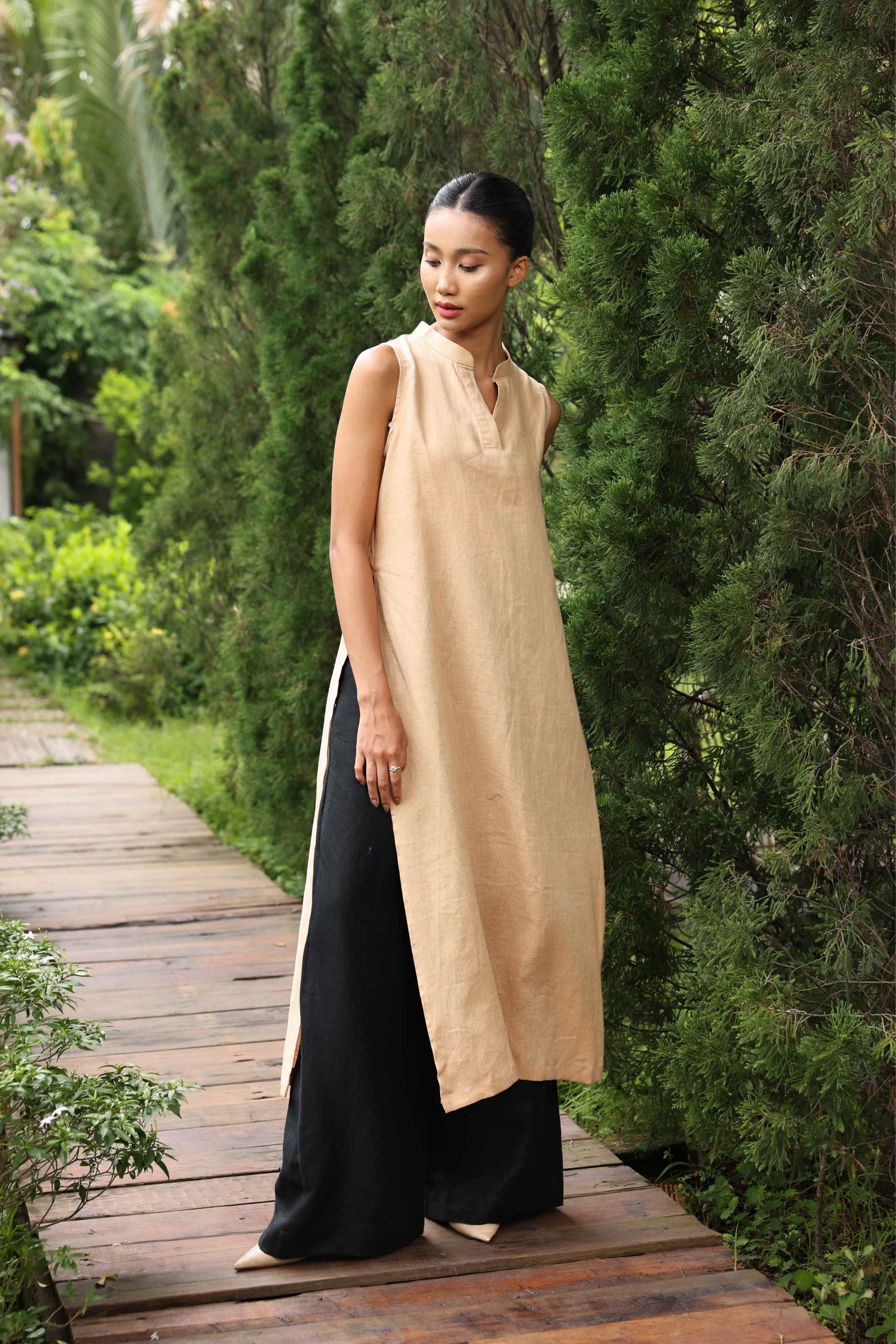 Woman wearing a beige and black dress standing on a wooden path in a garden.