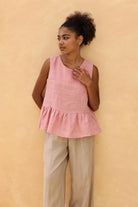 Woman wearing a pink sleeveless top with a peplum waist against a beige background