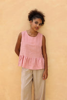Woman wearing a pink sleeveless top and beige pants against a beige background