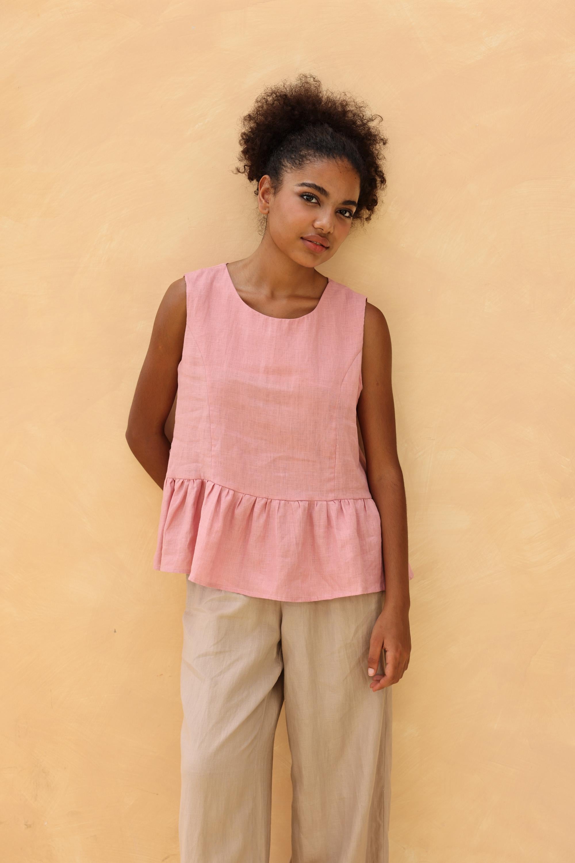 Woman wearing a pink sleeveless top and beige pants against a beige background