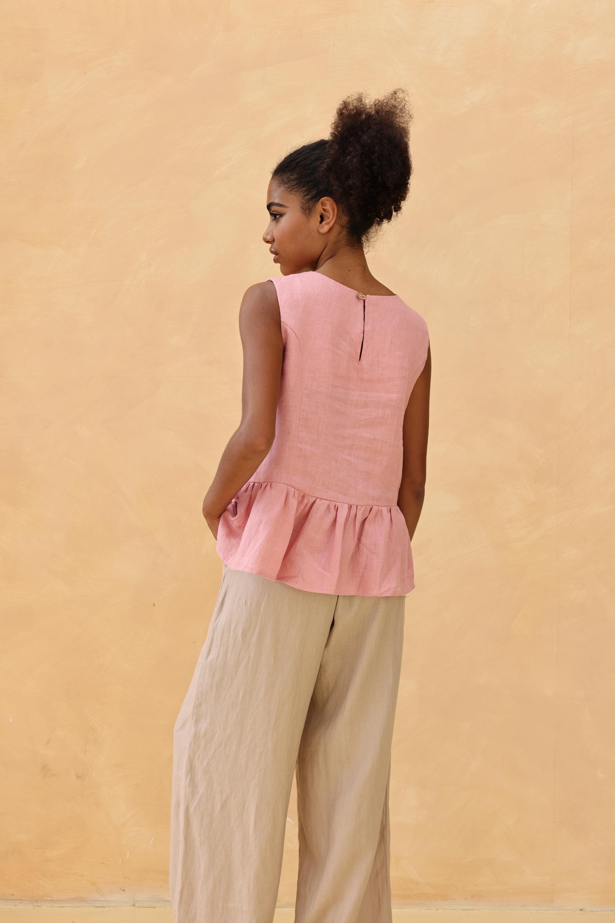Woman wearing a pink sleeveless top and beige pants against a beige wall
