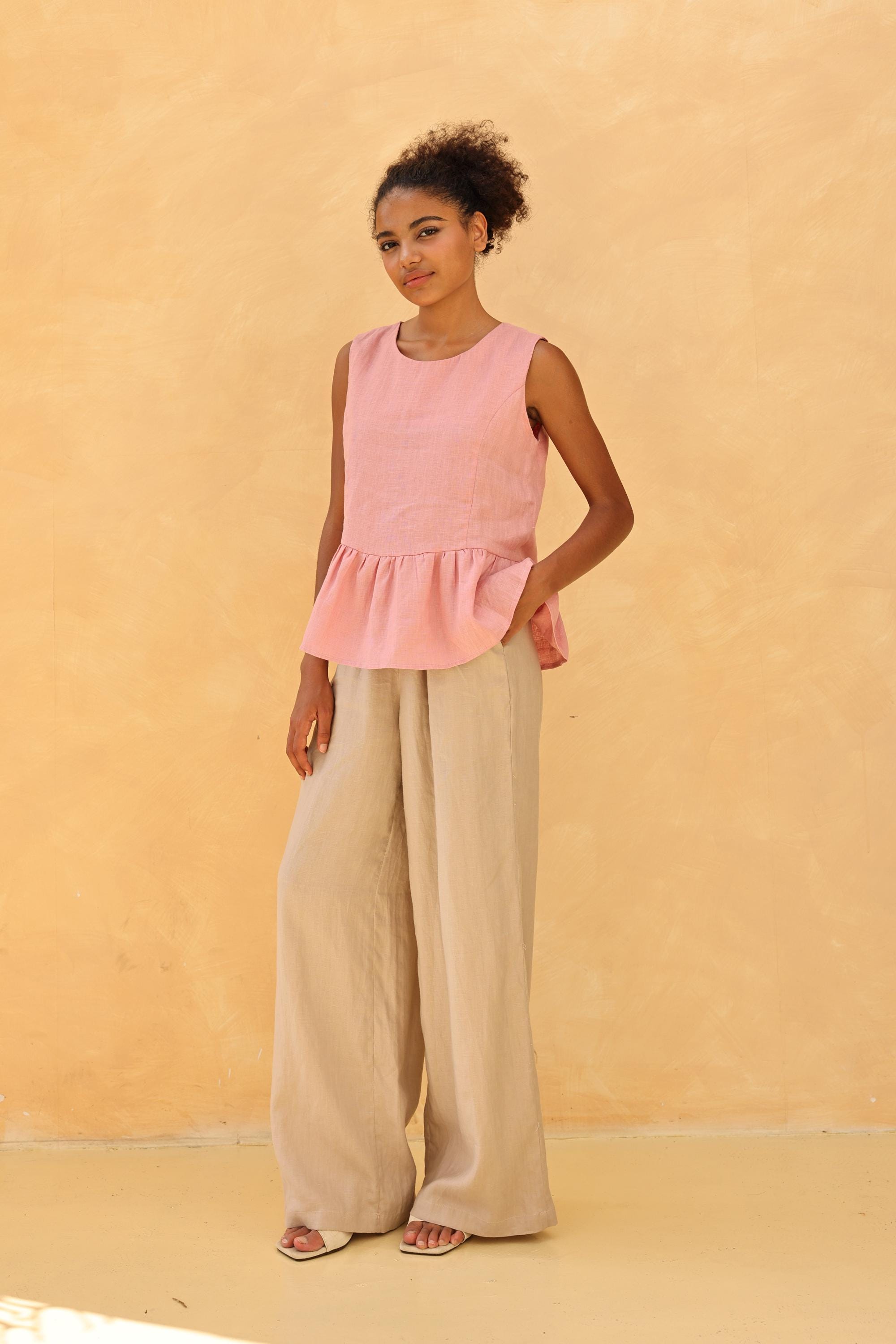 Woman wearing a pink sleeveless top and beige wide-leg pants against a beige background