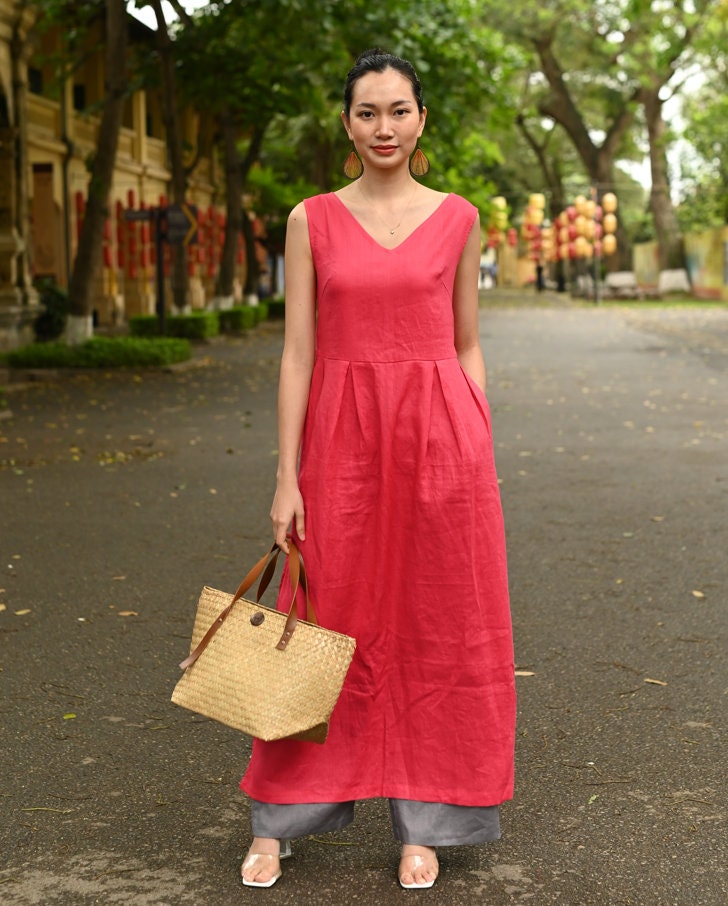 Woman in a red dress holding a straw bag on a tree-lined street.