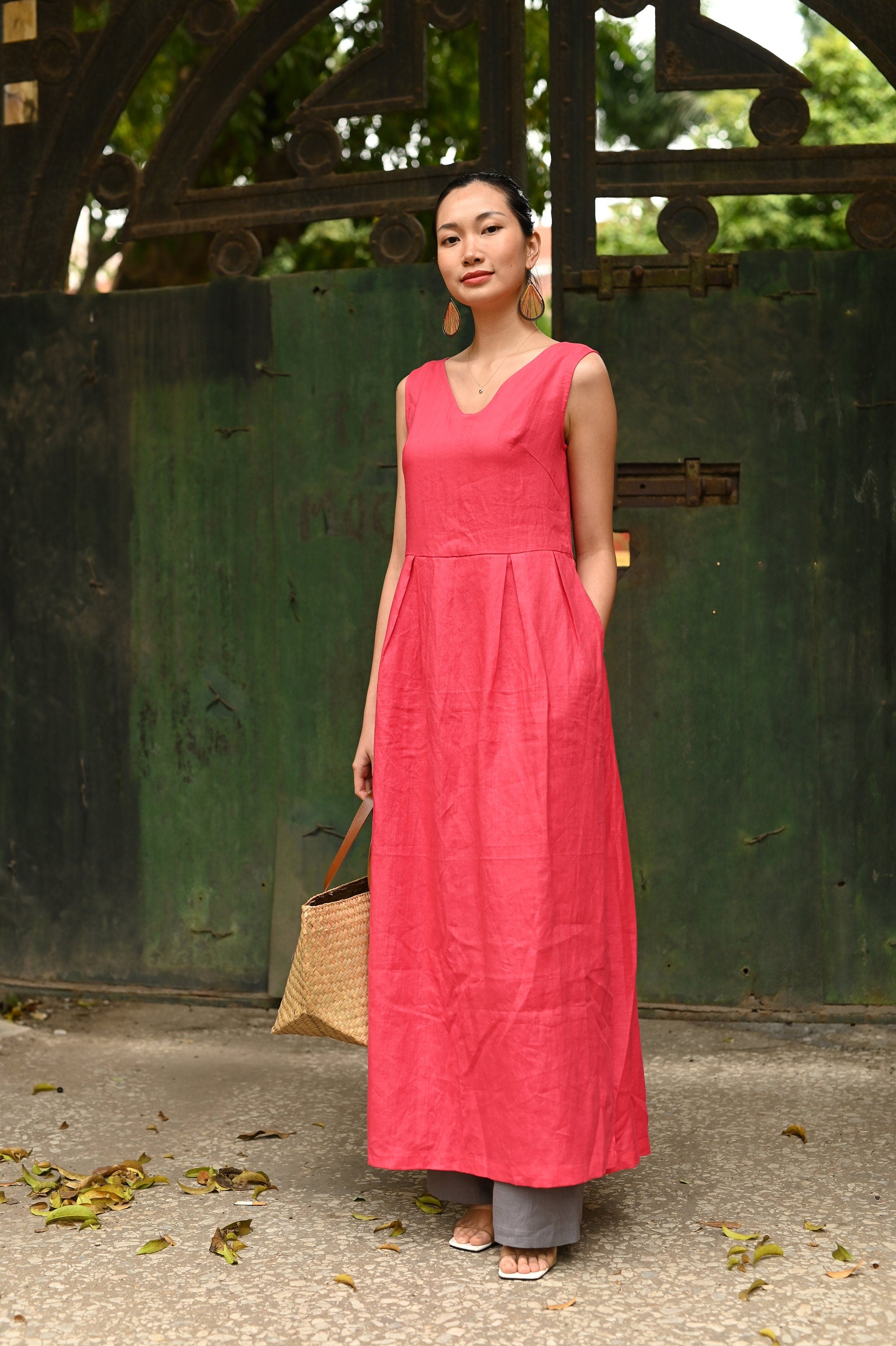 Woman in a long pink dress standing in front of a green metal gate.