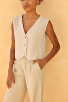 Person wearing a beige vest and pants against a beige background