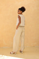 Woman wearing a sleeveless top and beige pants against a beige wall.