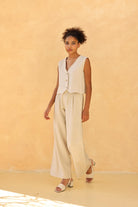 Woman wearing a cream-colored sleeveless top and wide-leg pants against a beige background