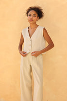 Woman wearing a beige vest and pants against a yellow background