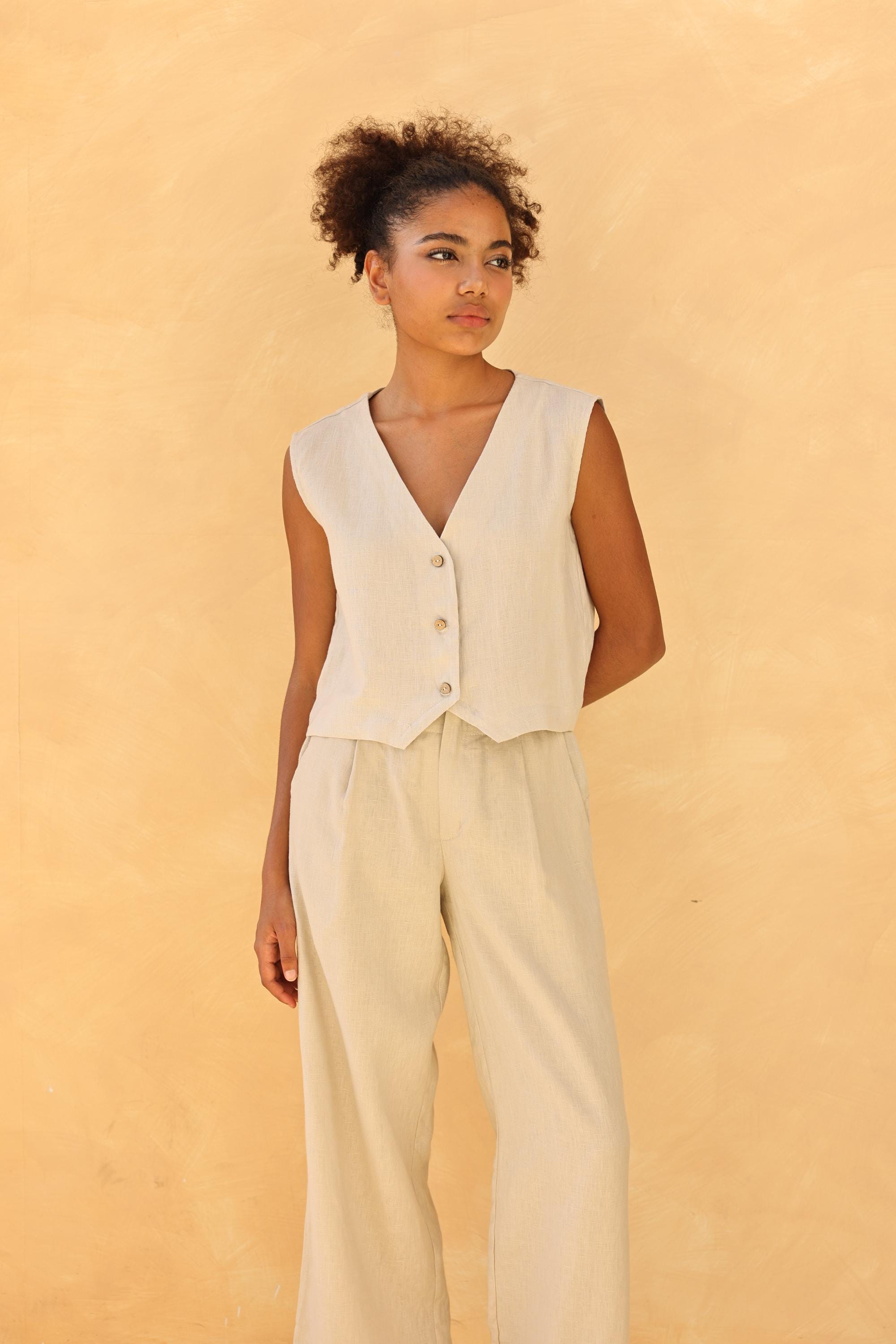 Woman wearing a vest over a beige top with wide-leg pants against a beige background