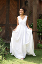 Woman in a white dress standing outdoors with wooden doors and greenery in the background