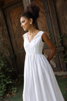 Woman in a white dress standing outdoors with wooden and stone wall background