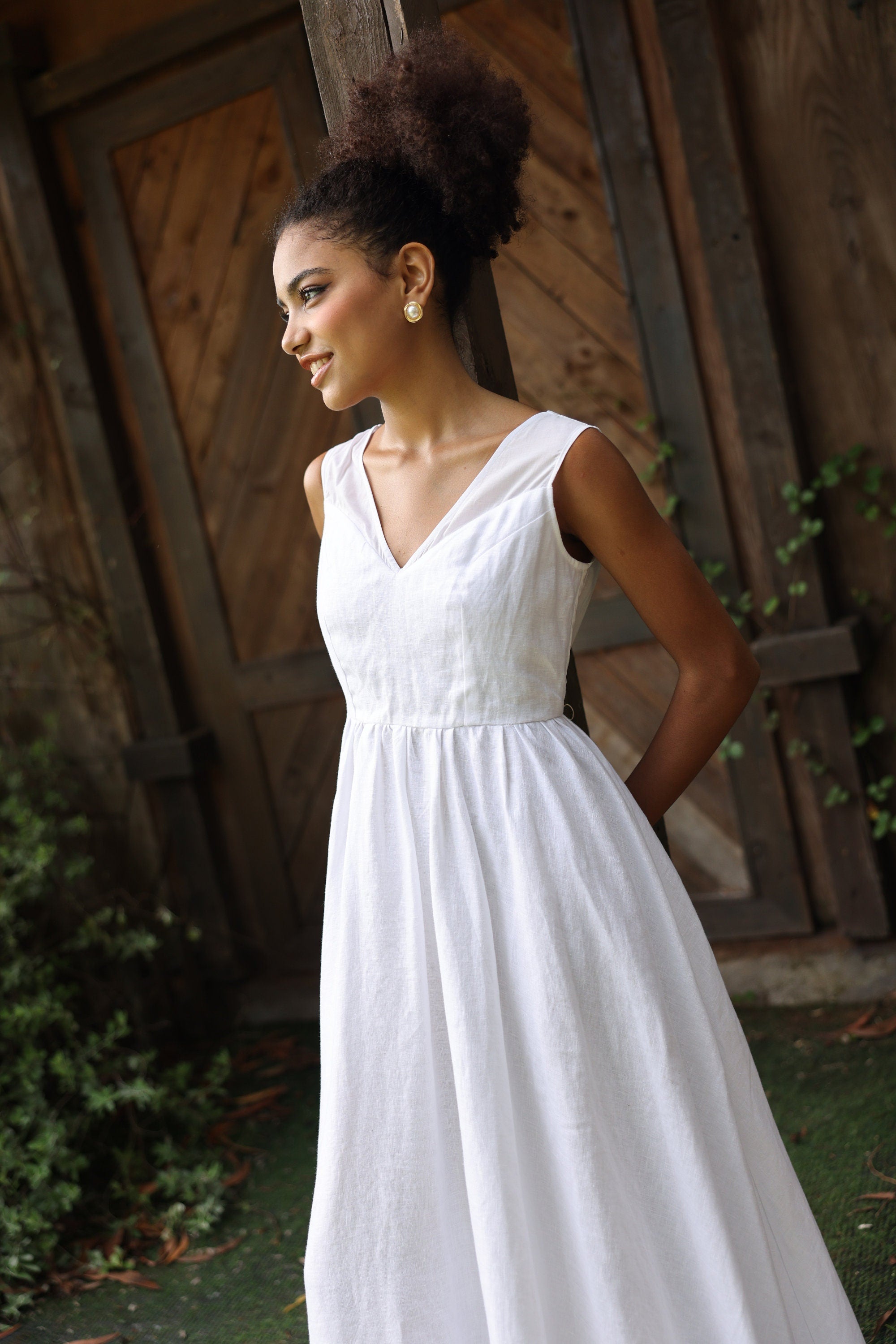 Woman in a white dress standing outdoors with wooden and stone wall background